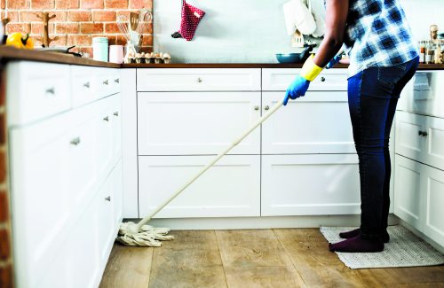 woman wearing blue jeans and plaid shirt, mopping her kitchen floor