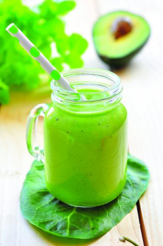 a green smoothie in a mason jar glass, with a green polka-dot straw, sitting on a leaf.
